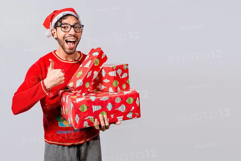 Smiling guy in christmas hat holding christmas gift boxes giving thumbs up. Friendly man in christmas clothes holding gift boxes, Christmas man holding gift boxes and smiling with thumb up