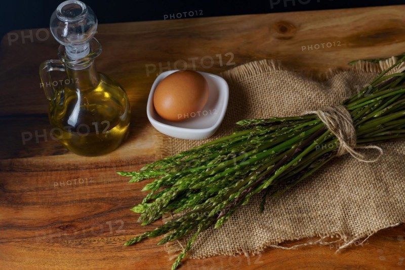 Bunch of wild asparagus on a raffia cloth with a jar of olive oil and eggs black background