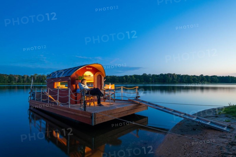 Man sitting in the blue hour on a houseboat, house raft, in front of the island Kiehnwerder, Breitlingsee, Brandenburg an der Havel, Havelland, Brandenburg, Germany, Europe
