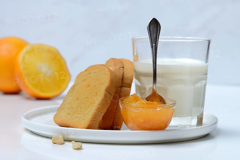 Rusk, glass of milk and orange marmalade in small bowls