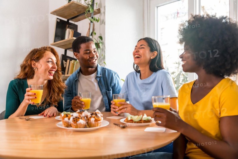 Multiethnic friends having breakfast with orange juice and muffins at home