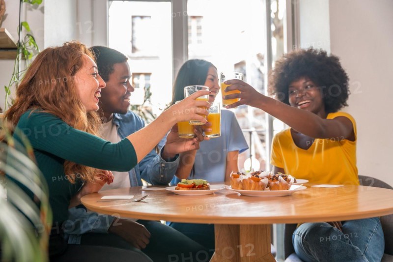 Multi-ethnic friends toasting over breakfast with orange juice and muffins at home