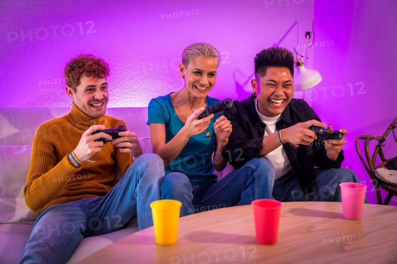 Group of young friends play video games together on the sofa at home, purple led