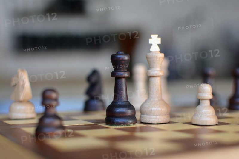 Chess board game with focus on black and white queen pieces on blurry