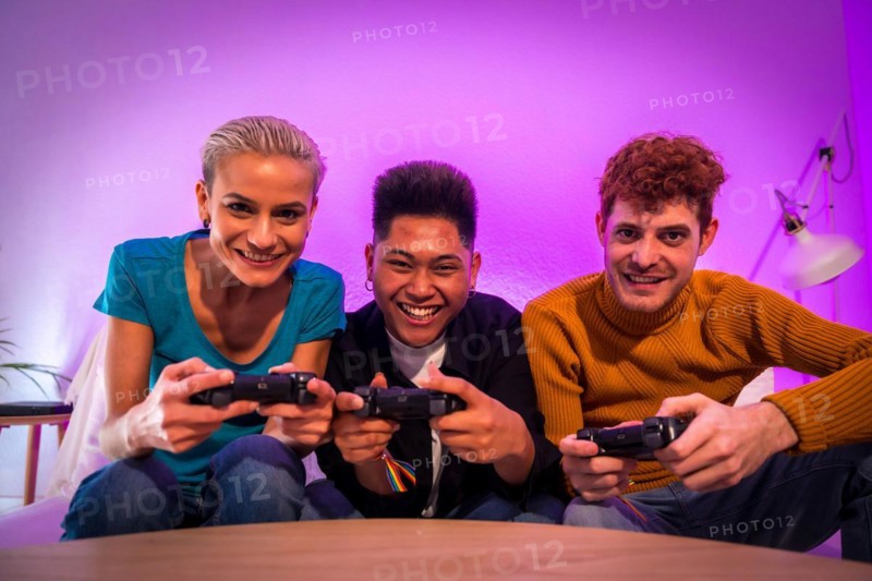 Group of young friends playing video games together on the sofa at home, purple led, competing looking at camera