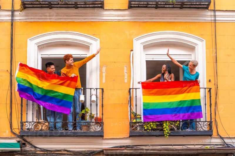 Couples of gay boys and lesbian girls with the lgtb flag on the balconies at a house party, greeting friends