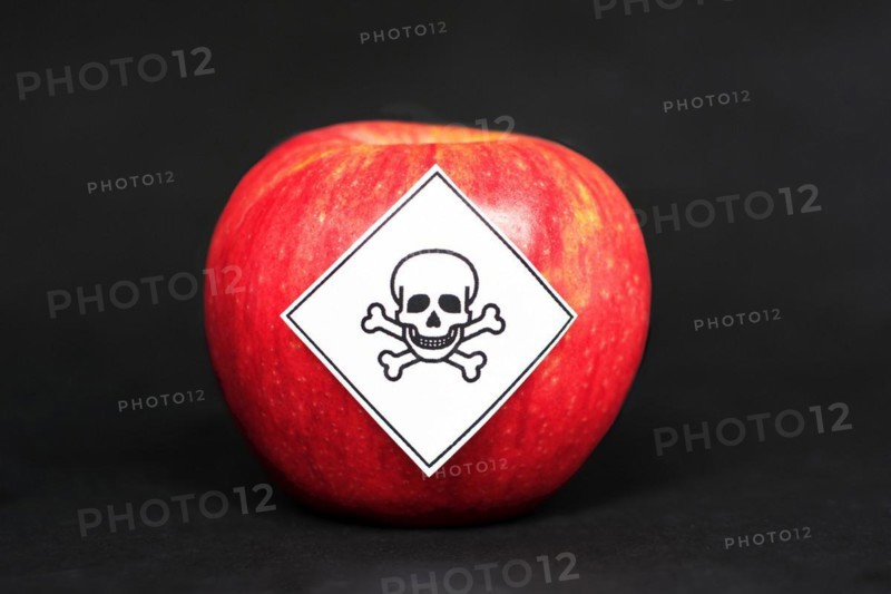 Concept of pesticide residues in agricultural food products dangerous to humans, showing a red apple with poison symbol sticker on black background