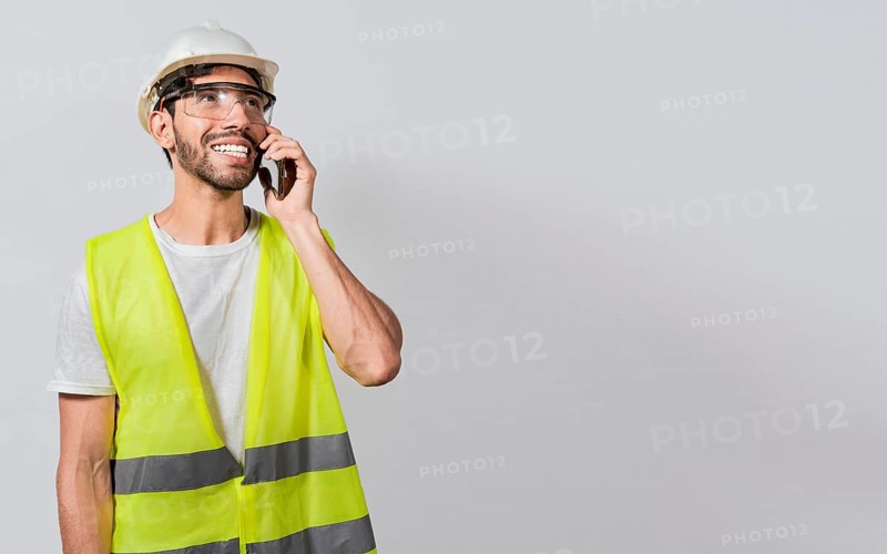 Young builder engineer in vest talking on cell phone isolated. Civil engineer concept talking on cellphone isolated, Smiling engineer talking on the phone isolated with copy space