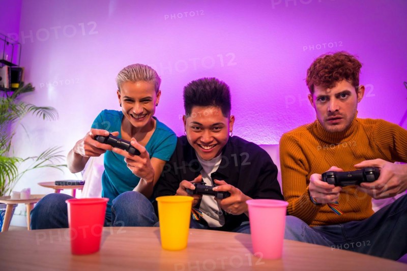 Group of young friends playing video games together on the sofa at home, portrait looking at camera