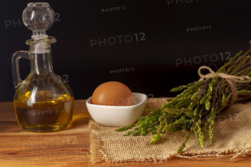 Bunch of wild asparagus on a raffia cloth with a jar of olive oil and eggs black background