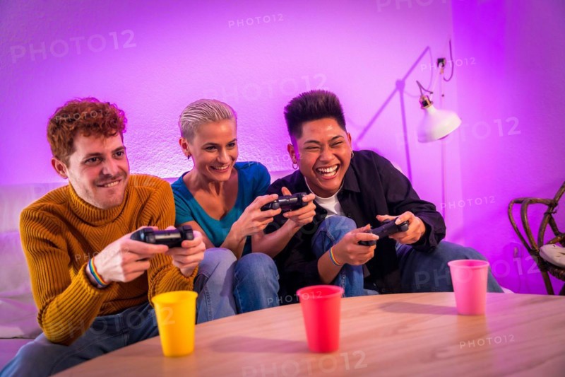 Group of young friends playing video games together on the sofa at home, purple led, having fun