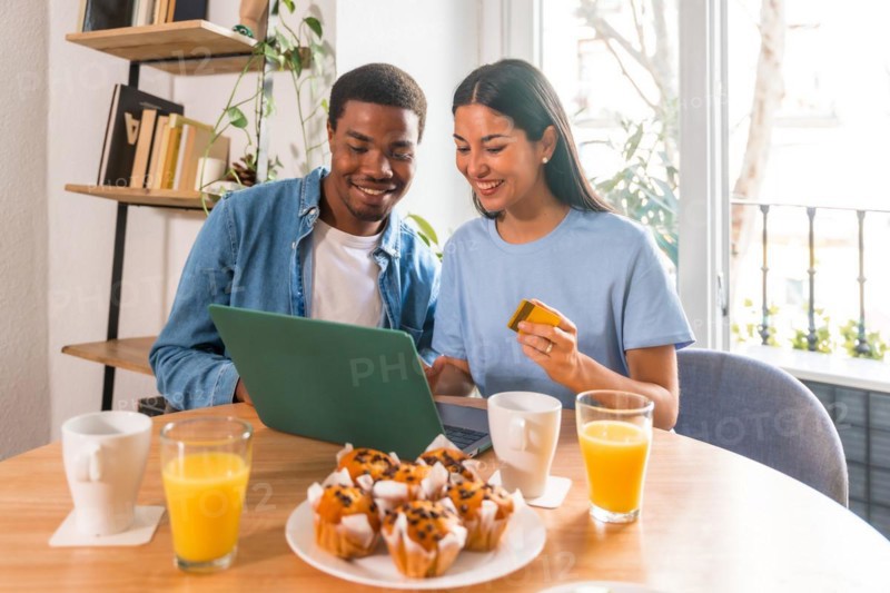 Couple making purchase online with the computer while having breakfast, next to the window, shopping on the internet