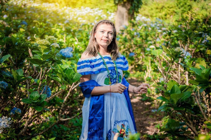Smiling woman in national folk costume in a field surrounded by flowers. Nicaraguan national folk costume