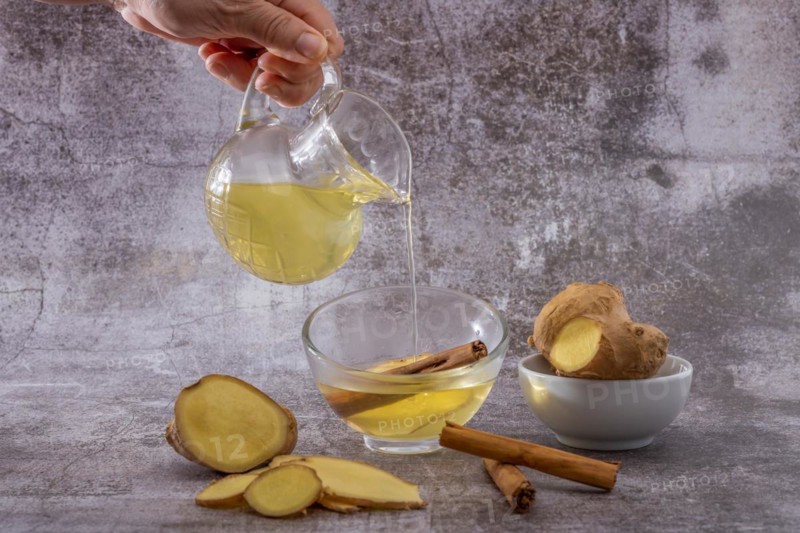 Womans hand pouring a cup of fresh ginger tea with cinnamon and lemon