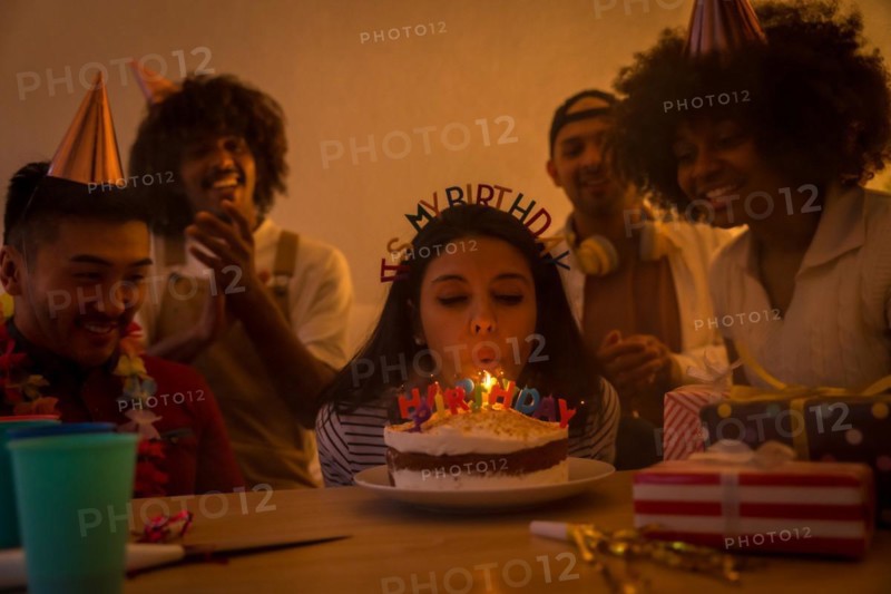 Multi-ethnic group of friends at a birthday party on the sofa at home with a cake and gifts