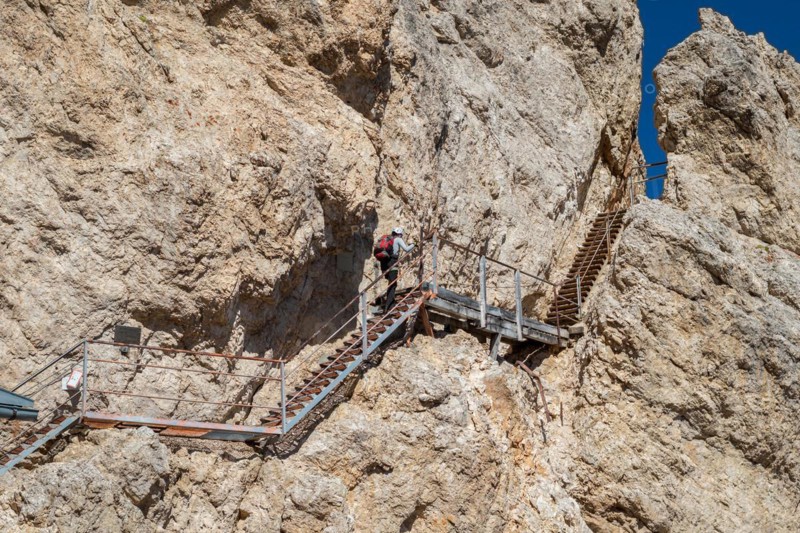Tourist climbing steel stairs fixed to the rock. Dolomites