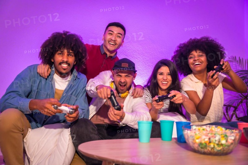 Adult party. Attractive young men sitting on the sofa playing video games with popcorn. Expressing joy while holding the joystick and looking at the monitor