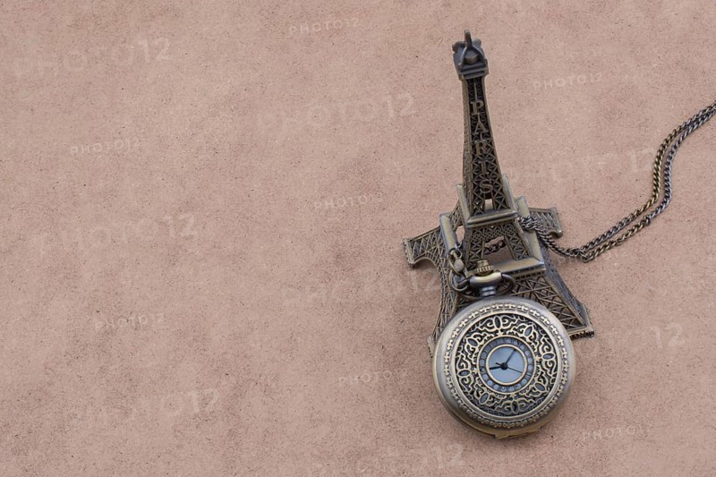 Little model Eiffel Tower and a pocket watch on brown background
