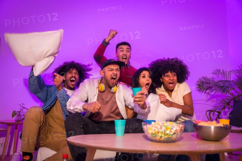 Adult party. Young people sitting on the sofa watching a football game with popcorn. Emotion for soccer