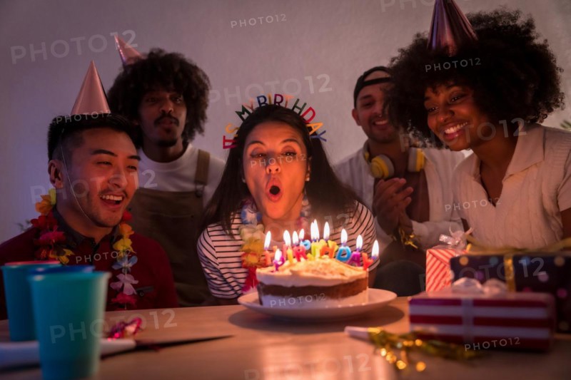 Multi-ethnic group of friends at a birthday party on the sofa at home with a cake and gifts