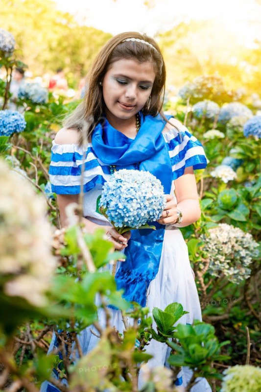 Beautiful Nicaraguan woman in national folk costume holding flowers in a nursery. Portrait of girl in traditional Central American folk costume holding flowers in a nursery. Nicaraguan folk costume