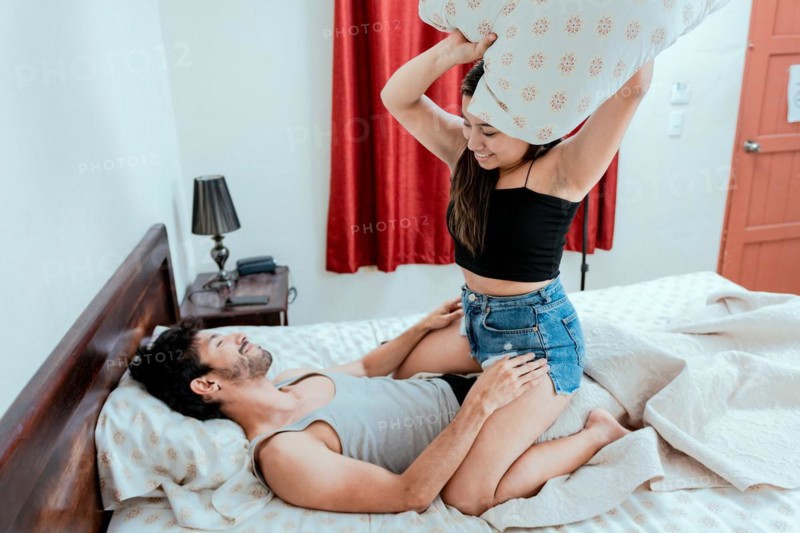 Young couple playing with pillow in bed. Couple in love playing with pillow in bed