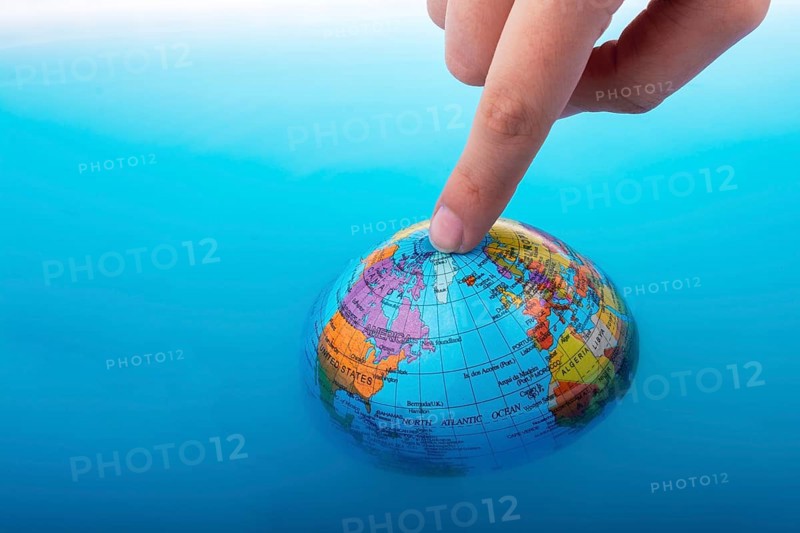 Little globe with finger on top floating in blue water