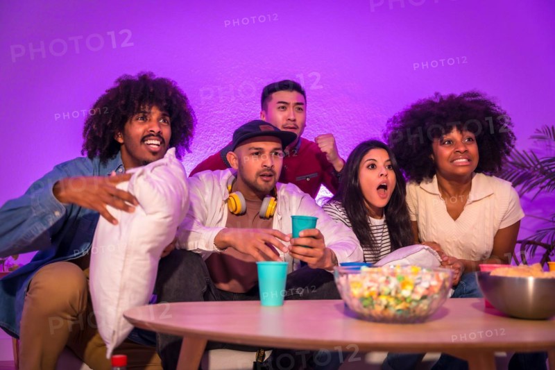 Adult party. Young people sitting on the sofa watching a football game with popcorn. Excitement for soccer