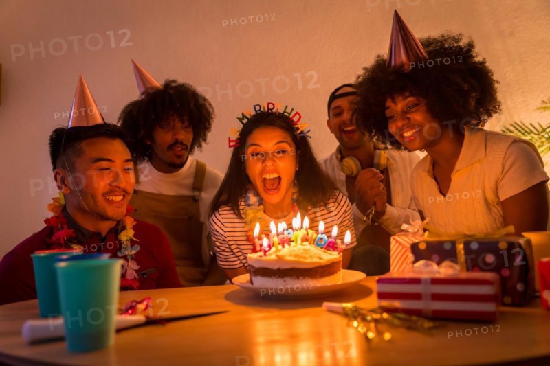 Multi-ethnic group of friends at a birthday party on the sofa at home with a cake and gifts