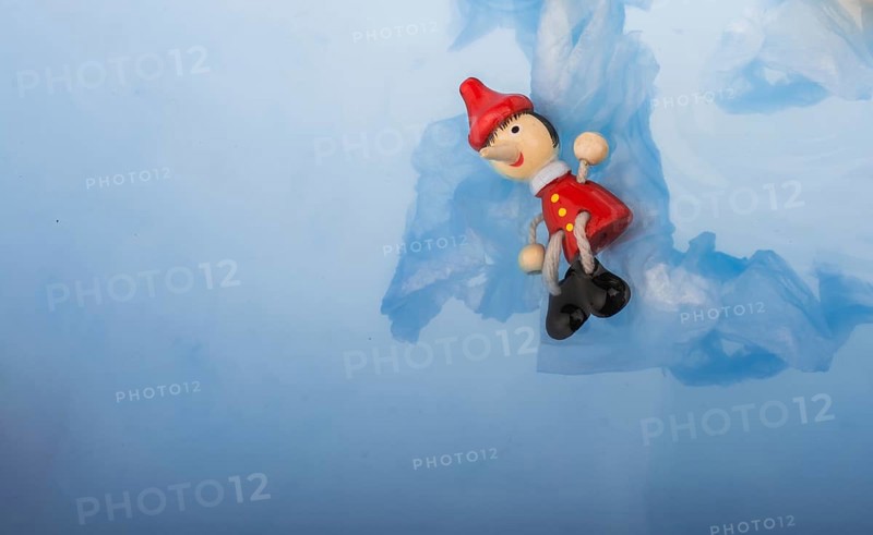 Hand holding wodden puppet Pinocchio on in blue water
