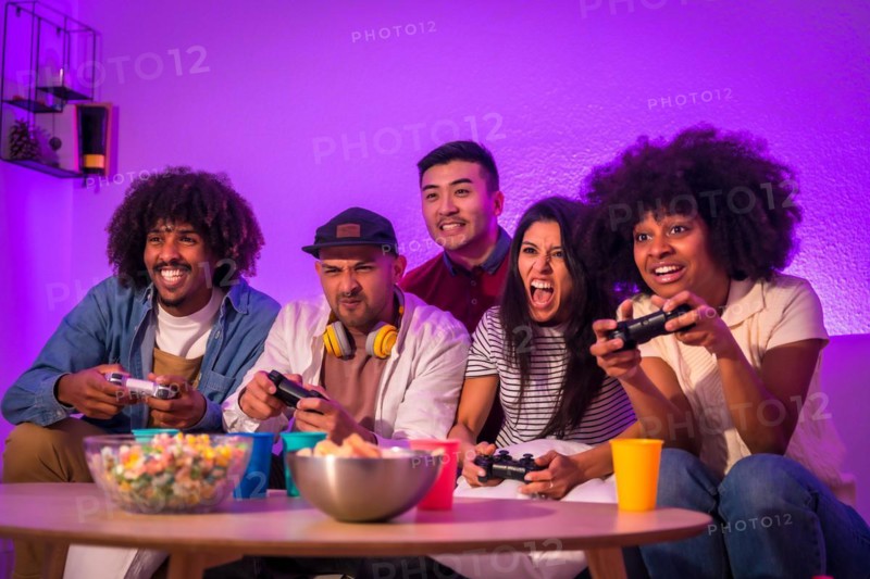 Adult party. Young people sitting on the sofa playing video games with popcorn. Joystick or controller in hand