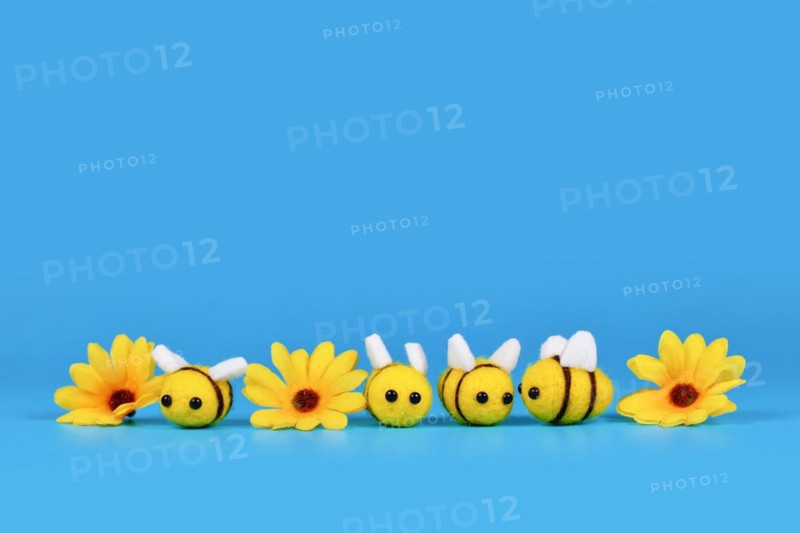 Cute felt bees and yellow flowers in a row on blue background with copy space