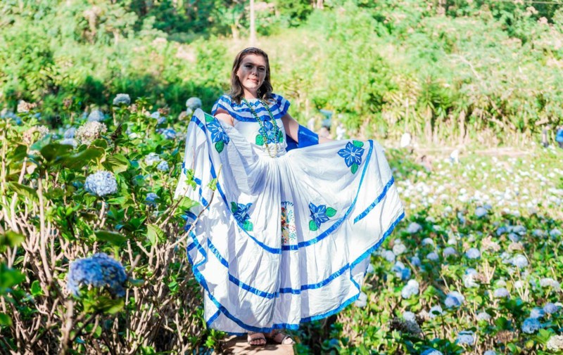 Smiling woman in national folk costume in a field surrounded by flowers. People in Nicaraguan national folk costume. Young Nicaraguan woman in traditional folk costume in a field of Milflores