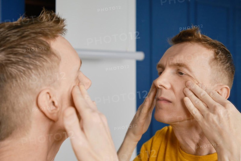 Concentrated man massaging and rubbing lotion under his eyes. Male aging problem