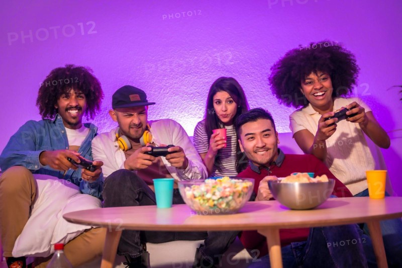 Adult party. Attractive young men sitting on the sofa playing video games. Expressing joy while holding the joystick and looking at the monitor