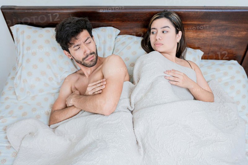 Upset couple in bed with crossed arms. Woman lying in bed upset with her husband. Angry man and woman in bed with crossed arms. Marriage problems concept