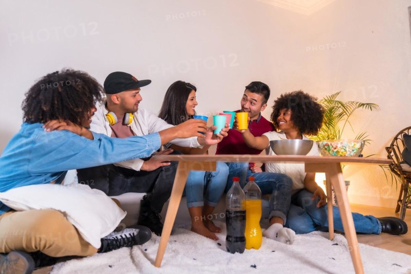 Group of friends eating popcorn and toasting with soft drinks. Laughing while watching a funny movie on TV at home