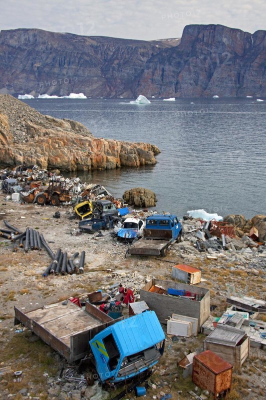 Rubbish and car wrecks at garbage dump and icebergs at the fishing village Uummannaq
