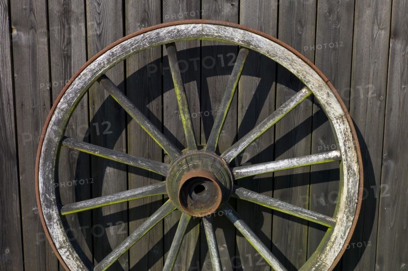Wooden wagon wheel leaning against a shed wall