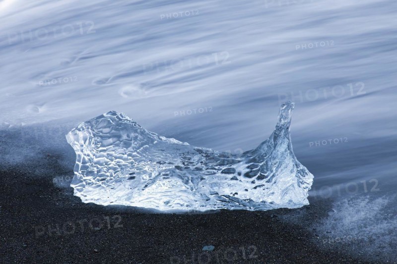 Melting block of ice washed on beach along the Atlantic Ocean coastline at Breidamerkursandur black sands in winter
