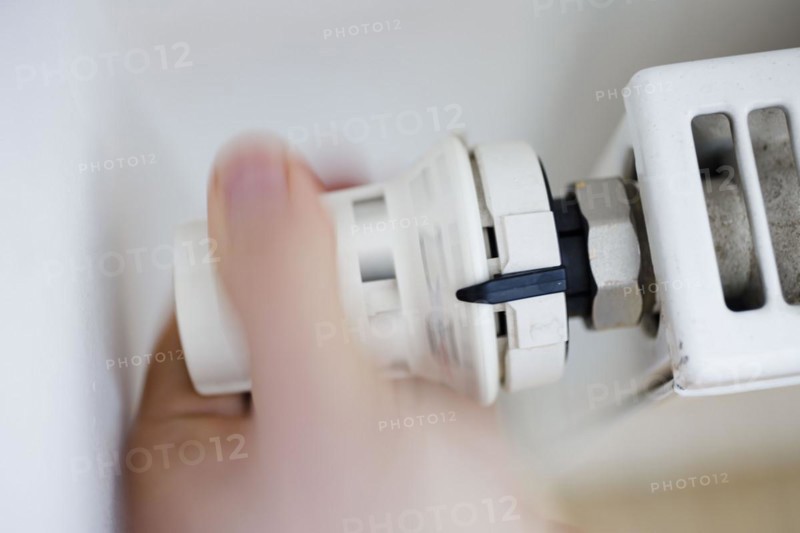 Symbolic photo on the subject of increased heating costs. A person turns the thermostat of a heating system. To save on heating costs