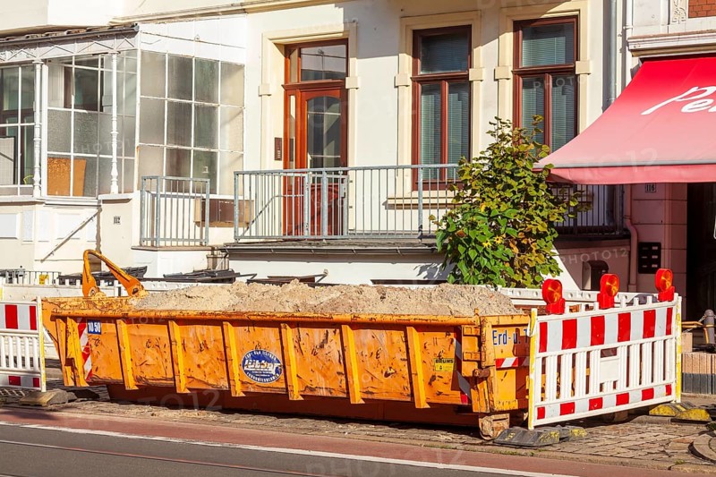 Orange skip for construction waste standing on the road in front of residential buildings