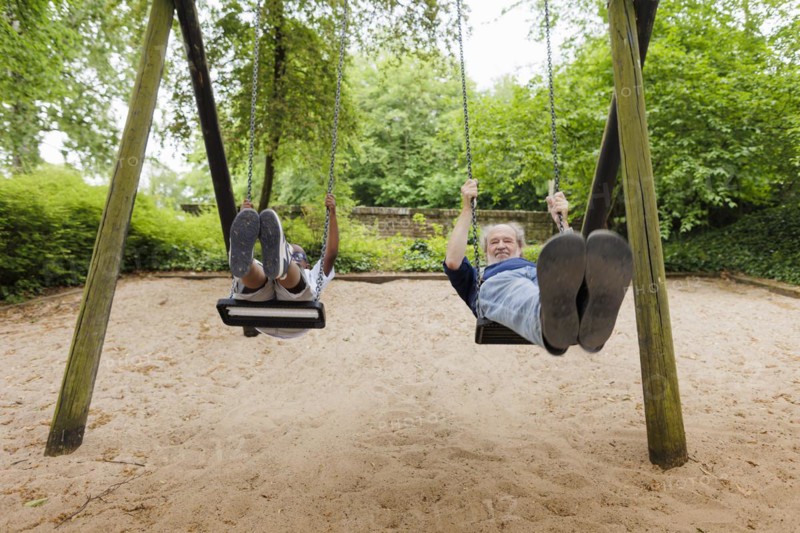 Temporary grandparents. Grandfather swinging with his charge in a playground.