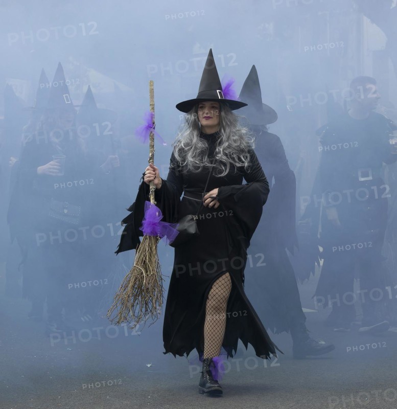 A witch in black and with a broom and behind everything in the smoky mist at the carnival in the city of Rijeka