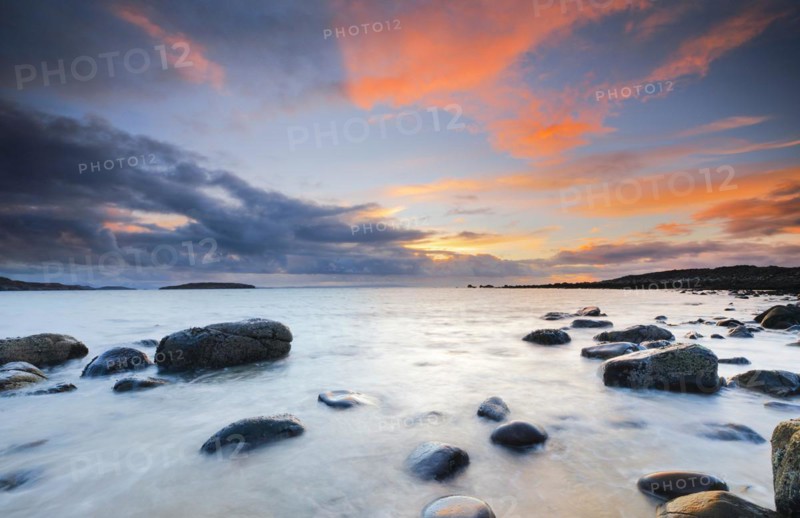 Orange coloured cloudy sky at sunset on a sandy beach strewn with round stones near Achiltibuie on the west coast of Scotland