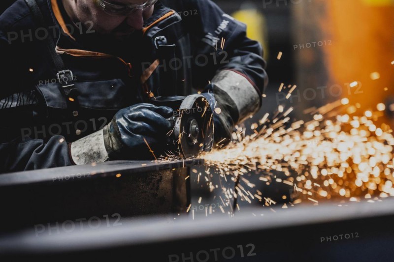 A metal worker works on a steel beam with a cut-off grinder