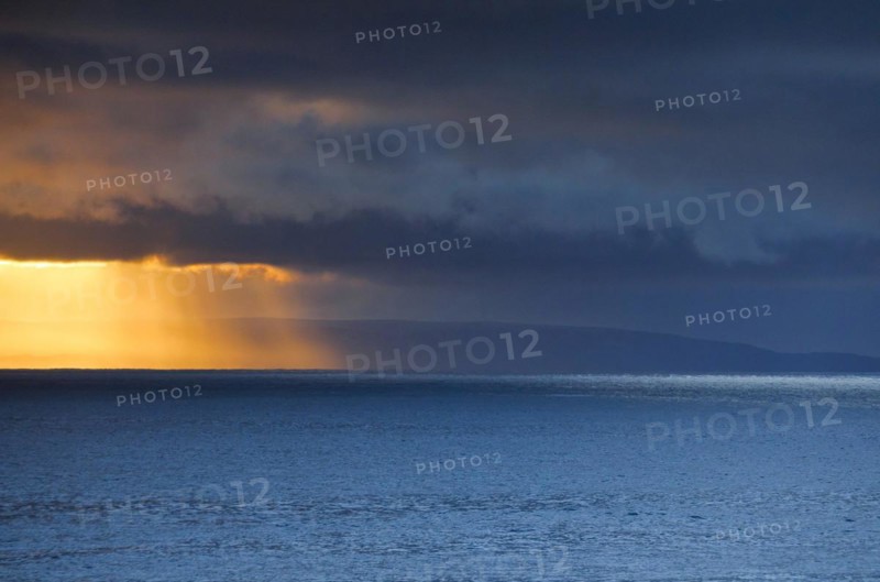 Evening sun breaks through low-lying rain clouds over the Summer Isles and the open waters of the blue Atlantic