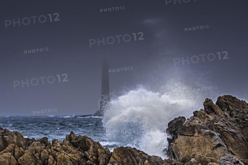 Wave crashing on rock and Phare de Goury lighthouse in the mist at dusk near Auderville