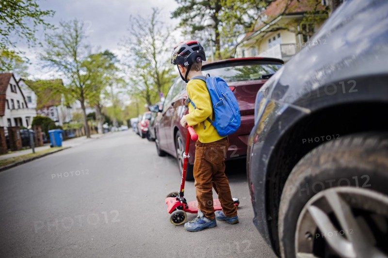 Symbolic photo on the subject of children in road traffic A little boy stands with his scooter between parked cars on a street. Berlin