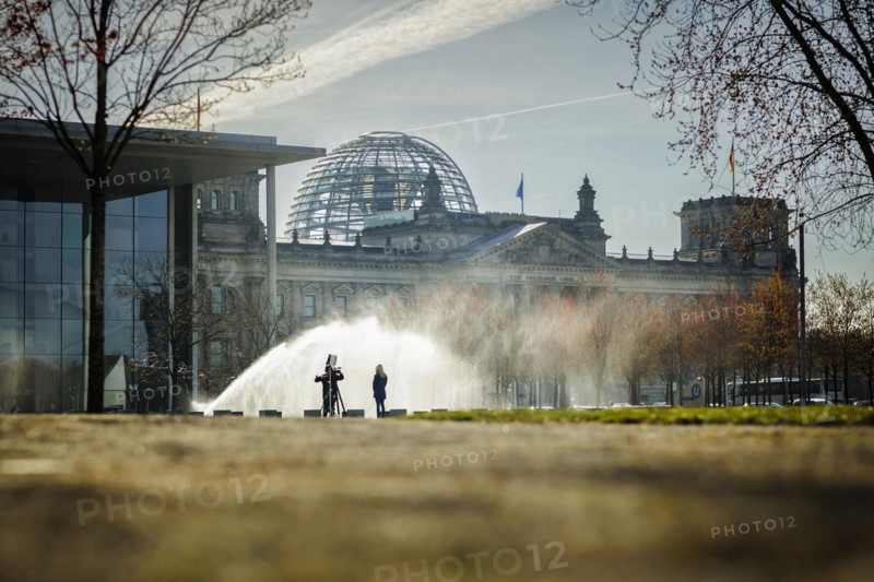 A water sprinkler waters a meadow in front of the Reichstag in the morning. Berlin